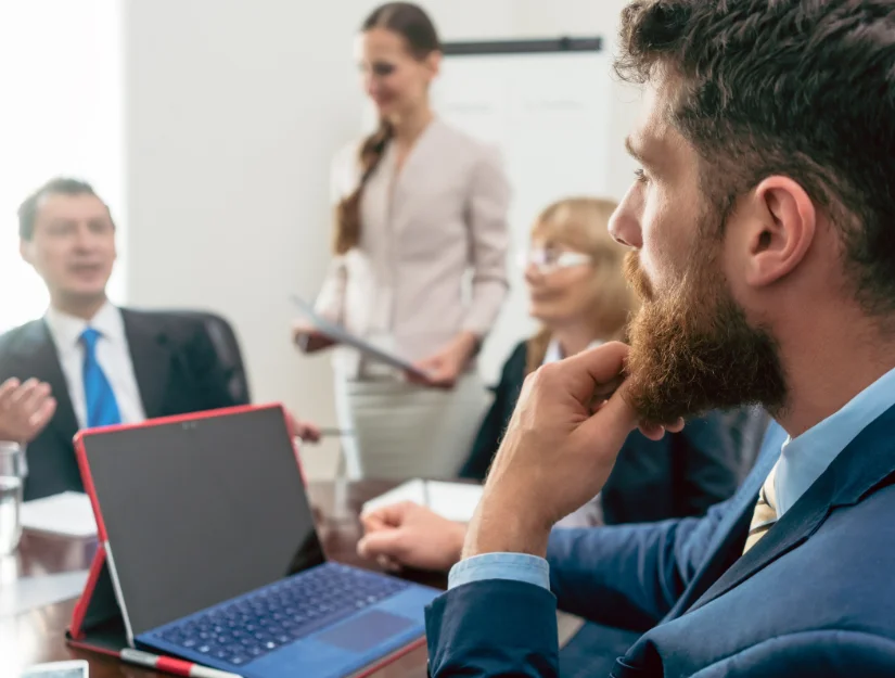 A professional meeting in progress, with a laptop on the table and attendees engaged in discussion, showcasing a modern office setting.