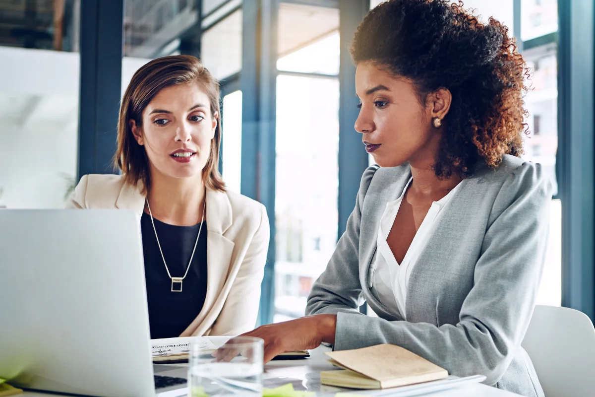 Two women in business attire analyzing information on a laptop.