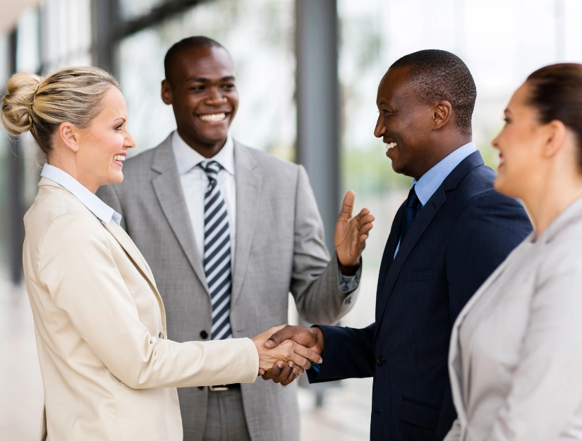 A group of four business professionals engaged in a handshake in a modern office setting.
