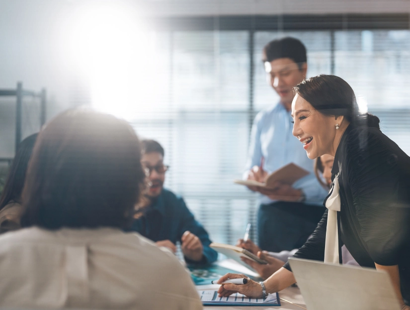 A Woman smiling while presenting Infront of her collogues in an office
