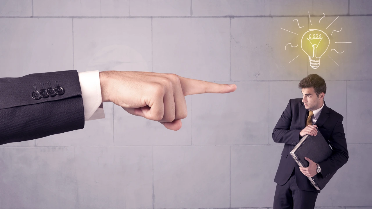 A hand points sternly at a businessman holding a folder, with a glowing light bulb illustration above his head, suggesting ideas or realization