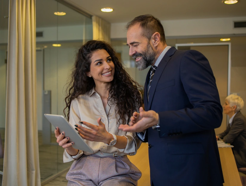 Two people in business attire having a conversation. One is holding a tablet.
