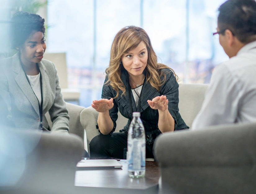 A group of professionals in a modern office engage in a discussion, with a focus on collaboration and communication. A water bottle is visible.