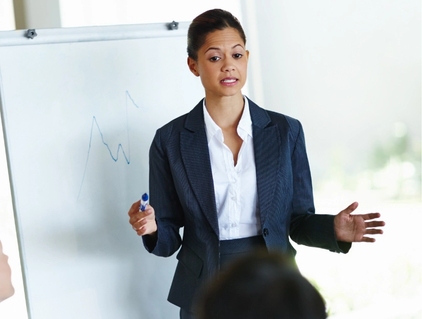 A business professional in a suit presenting in front of a whiteboard with a growth chart, engaging with an audience.