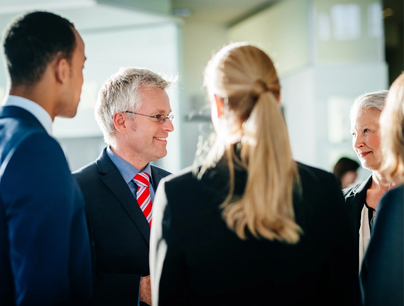 A group of four professionals in business attire engaging in a discussion in a bright, modern office setting.
