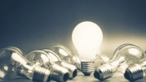 A glowing light bulb surrounded by scattered unlit light bulbs on a dark background, symbolizing inspiration and creativity.