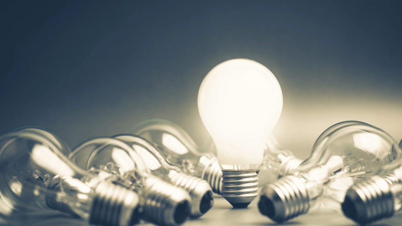 A glowing light bulb surrounded by scattered unlit light bulbs on a dark background, symbolizing inspiration and creativity.