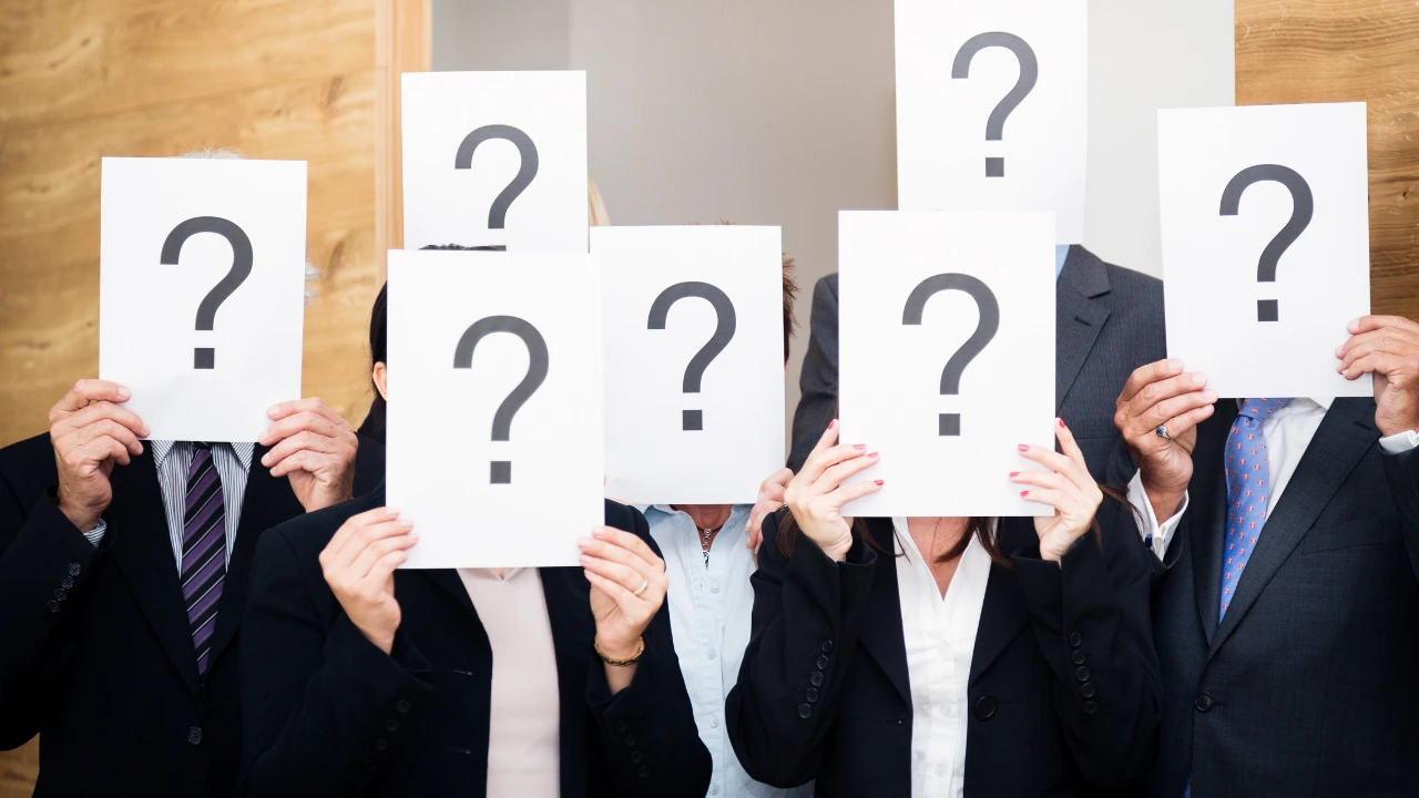 A group of people holding signs with question marks, obscuring their faces, expressing curiosity or uncertainty.
